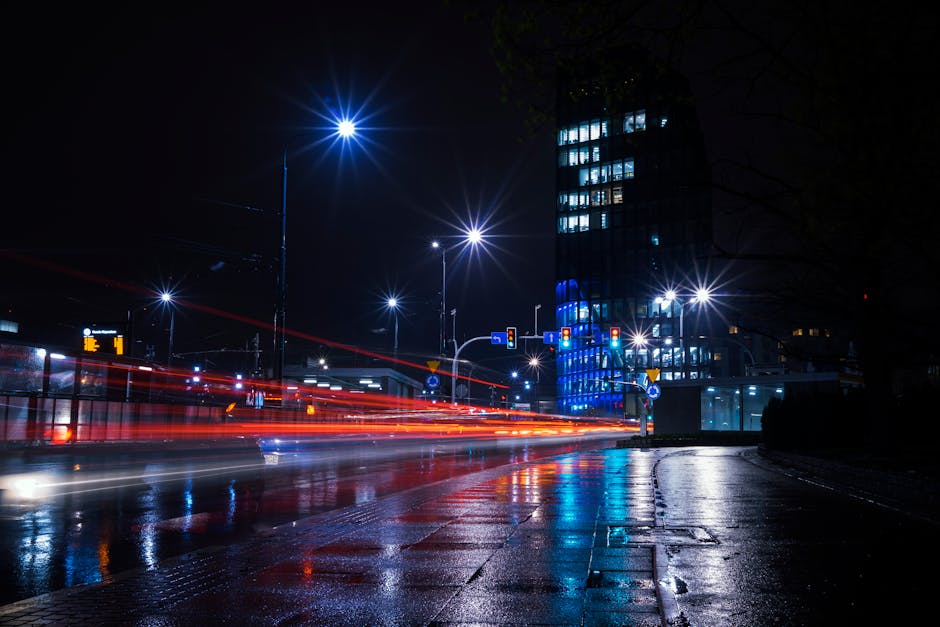 Illuminated city street at night with vibrant light trails and urban skyline.